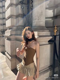 Woman in a brown corset top and beige mini skirt outdoors with sunlight