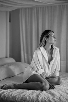 Woman in an unbuttoned white shirt sitting on a bed in a bedroom