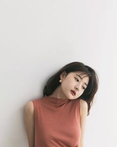 Woman with dark hair and a sleeveless top leaning against a white wall