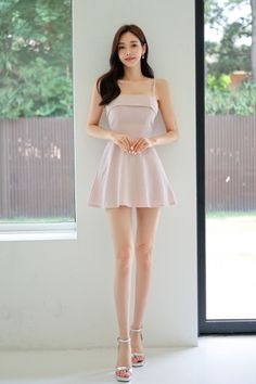 Woman in a pink dress and silver heels standing indoors by a window