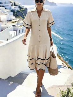 Woman in a cream dress and sunglasses walking down steps with an ocean view