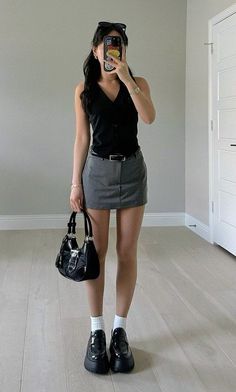 Woman in a black top and mini skirt taking a mirror selfie indoors