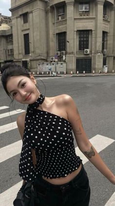 Woman in a polka dot one-shoulder top and black jeans on a city street