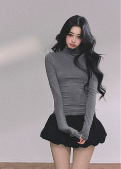 Woman with long black hair wearing a gray turtleneck and black mini skirt indoors