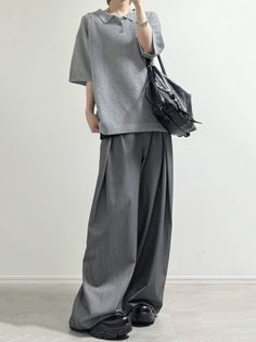 Person in a grey polo shirt and wide leg pants with a black bag