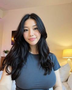 Woman with long black hair wearing a grey t-shirt in a bedroom