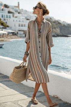 Woman in a striped dress and sunglasses walking along a sunny beachside promenade