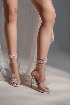 Woman wearing white high heels with rhinestone ankle wraps and a white dress