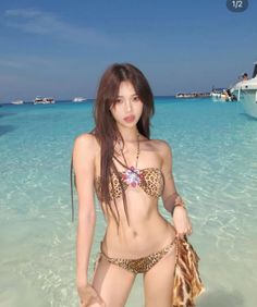 Woman in a leopard print bikini standing in clear beach water with boats in background