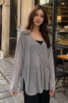 Woman with long brown hair wearing a grey cardigan and black top on a street