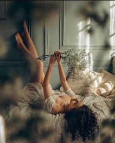 Woman with curly hair in a white dress lying on a bed with legs up