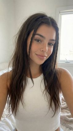 Woman with long hair and freckles wearing a white tank top indoors
