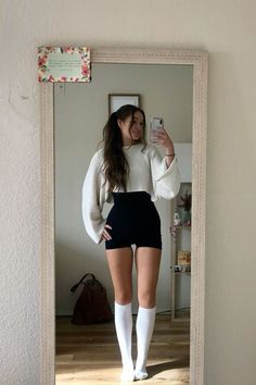 Woman in a cropped sweater and shorts taking a mirror selfie