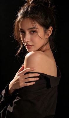 Woman with a messy bun and off-shoulder shirt against a dark background