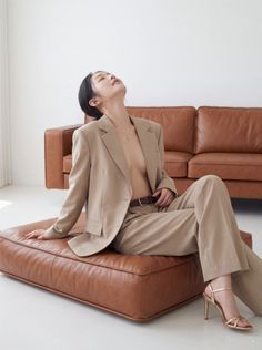 Woman in a beige suit and gold heels posing on a brown leather sofa