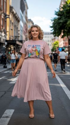 Woman in a pink t-shirt and pleated skirt standing on a city street