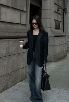 Woman in a black blazer and wide leg jeans walking on a street with a coffee cup