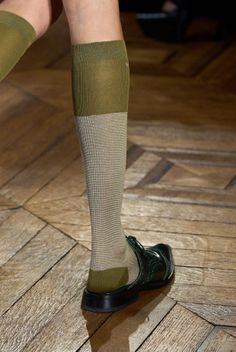 Leg wearing two-tone knee-high socks and dark dress shoes on a wooden floor