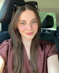 Woman with long brown hair and green eyes wearing sunglasses on her head in a car