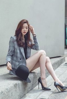 Woman in a plaid blazer and high heels sitting outdoors with a black hat