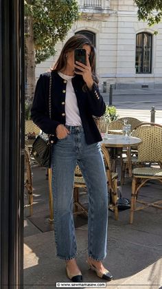 Woman in a navy blazer and blue jeans taking a mirror selfie at an outdoor cafe