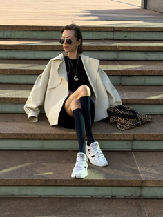 Woman in a black dress and white jacket sitting on outdoor steps