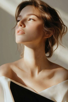 Woman with brown hair wearing an off-shoulder top in soft, warm lighting