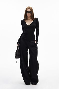 Woman in black long-sleeve top, wide-leg pants, and sunglasses holding a handbag