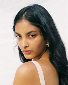 Woman with long black hair and gold earrings looking over her shoulder