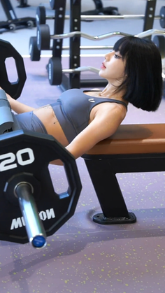 Woman with short black hair doing hip thrusts with a barbell in a gym