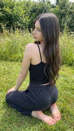 Young woman with long hair kneeling on grass in a black tank top and sweatpants