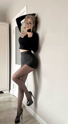 Woman in a black top and mini skirt posing for a mirror selfie