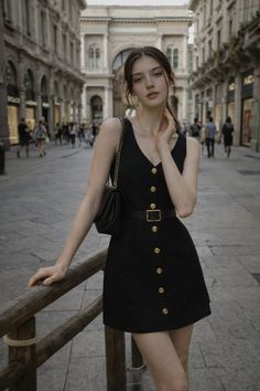 Woman in a black dress with gold buttons posing on a city street
