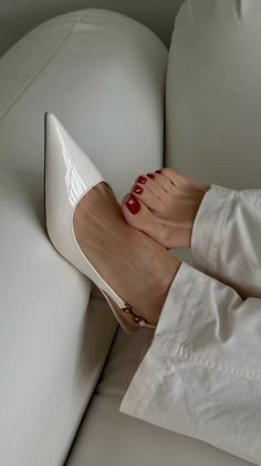 Feet with red nail polish and a white high heel shoe on a white couch