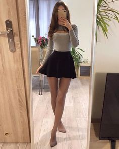 Woman in a mini skirt and long sleeve top taking a mirror selfie indoors