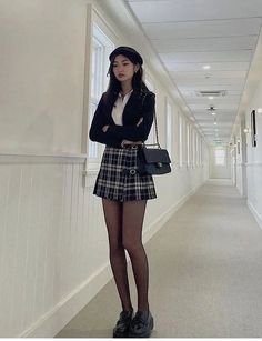 Woman in a plaid skirt, black blazer, and beret standing in a hallway