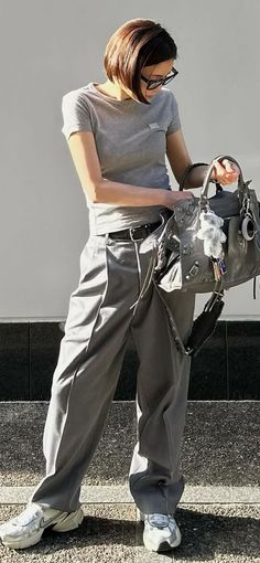 Person in gray t-shirt and pants holding a handbag outdoors