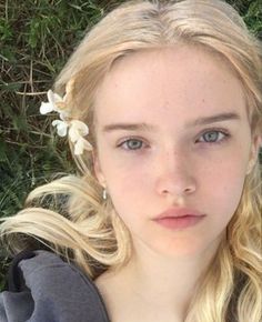 Young woman with blonde hair and white flowers in her hair, lying on grass