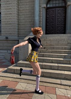 Woman in a school uniform running outdoors with a red handbag
