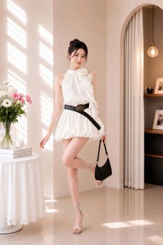 Woman in a white dress with a black belt and high heels posing indoors