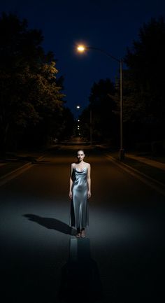 Woman in a silver dress standing on a dark street at night under a street light