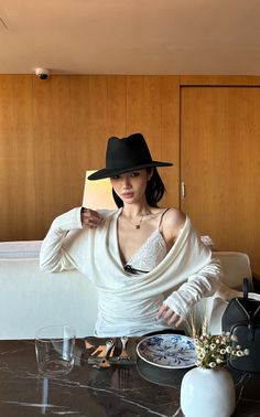 Woman in a black hat and white lace bra with a long sleeve top indoors