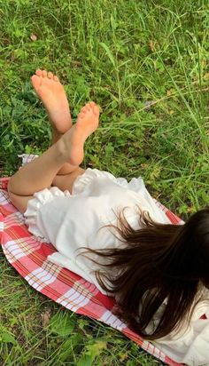 Person with long hair lying on a picnic blanket in the grass with bare feet up