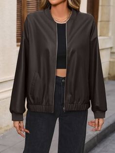 Woman in a dark brown bomber jacket and black crop top with jeans