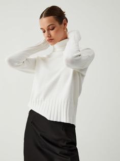 Woman in a white turtleneck and black skirt posing in a studio