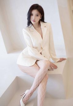 Woman in a white blazer and fishnet stockings posing indoors