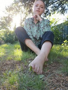 Woman in a floral shirt sitting barefoot on grass with sunlight in the background