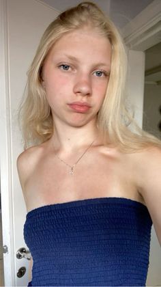 Young woman with blonde hair and blue eyes wearing a strapless top and cross necklace