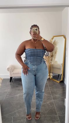 Woman in a houndstooth corset and light wash jeans taking a mirror selfie