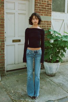 Woman in a black top and flared jeans standing outdoors